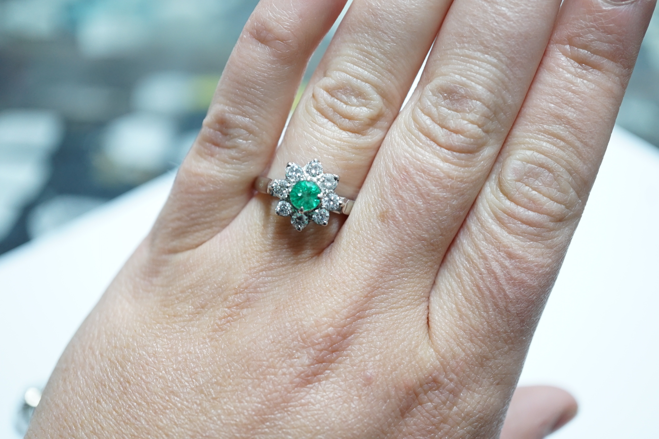 A modern 18k white metal, emerald and diamond set flower head cluster ring, size N, gross weight 4.5 grams.
